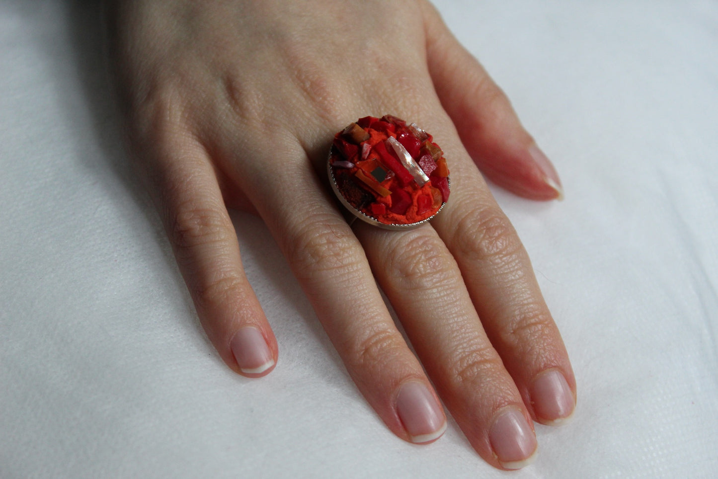 Anello in micromosaico rosso con specchietti su sfondo bianco indossato su mano