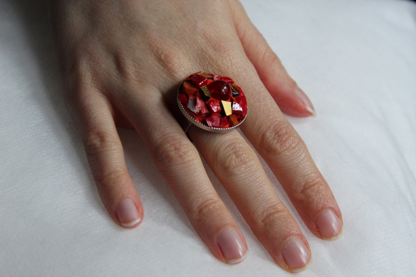 Anello in micromosaico rosso e oro con perla su sfondo bianco indossato su mano