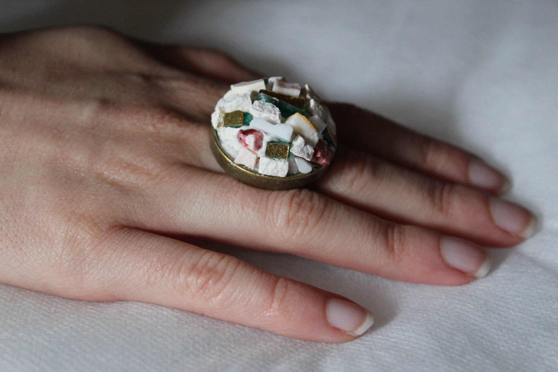 Anello in micromosaico bianco base ottone su sfondo bianco indossato su mano