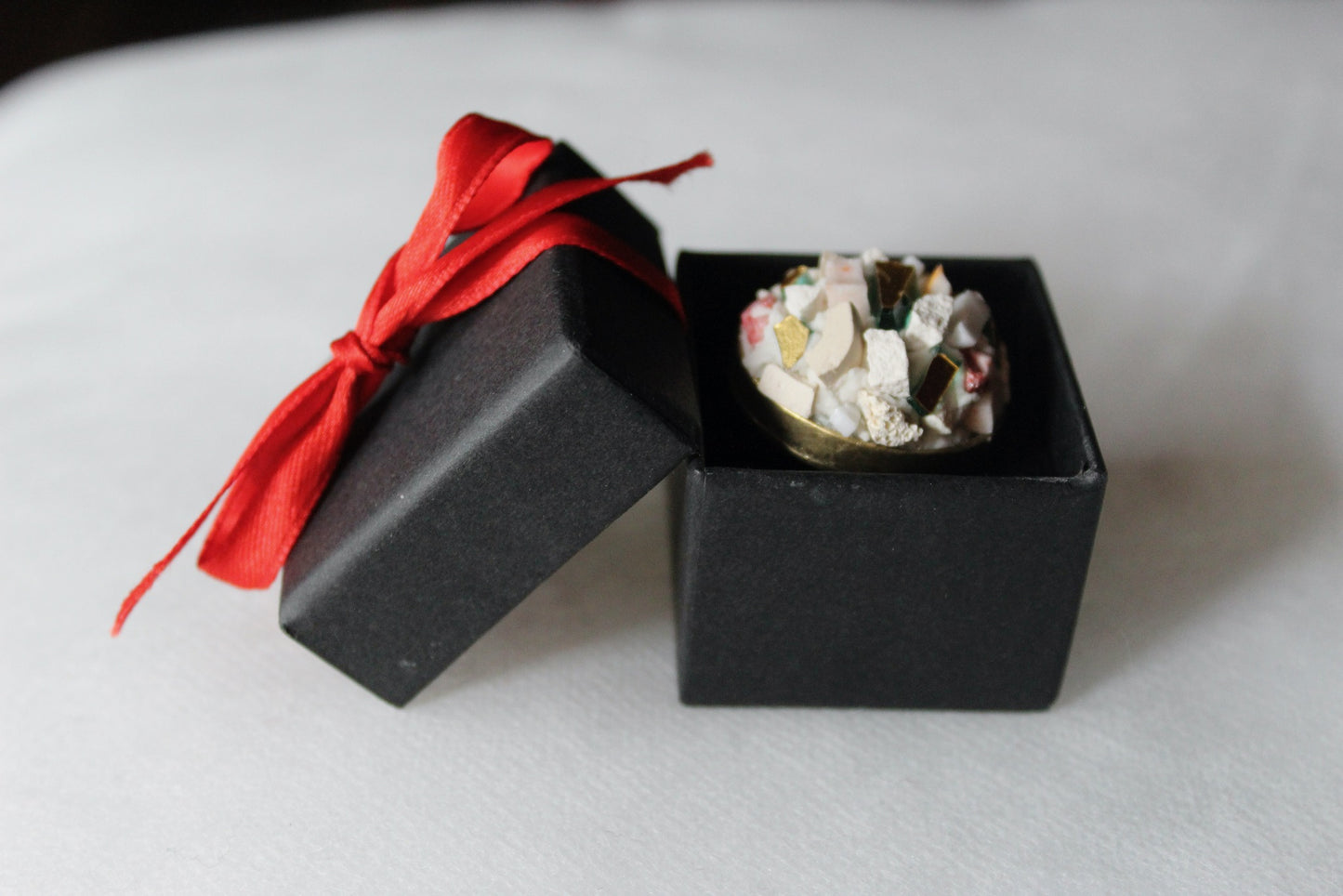 Anello in micromosaico bianco base ottone su sfondo bianco dentro scatolina nera con fiocco rosso