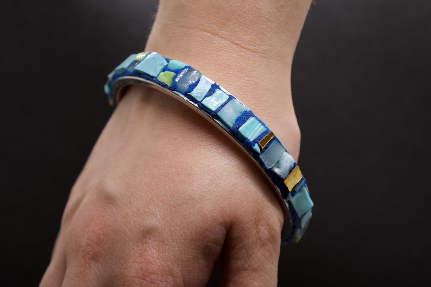 Bracciale micromosaico azzurro blu con oro puro su sfondo nero indossato sul polso