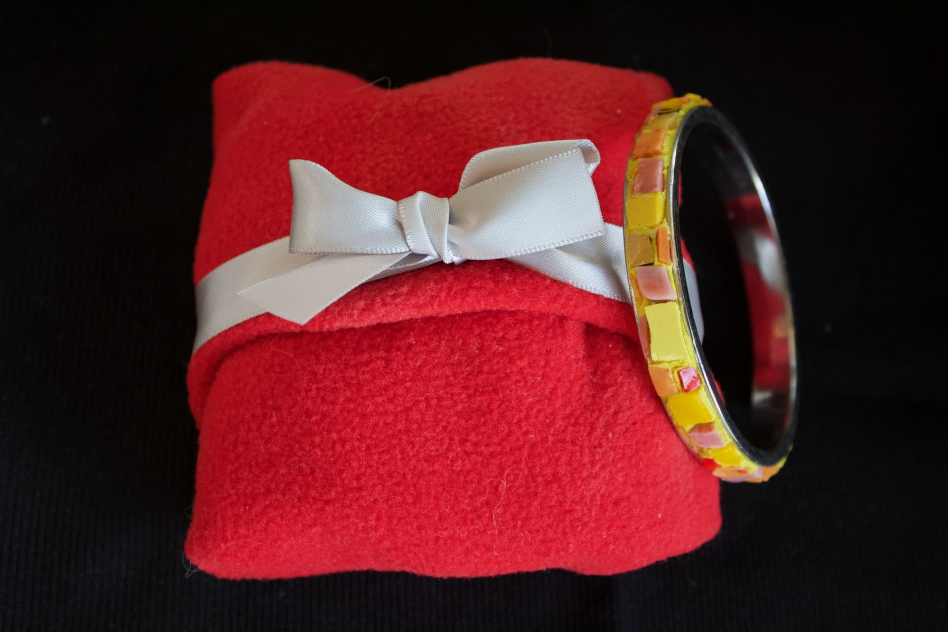 Bracciale giallo arancio in micromosaico su pacchetto in panno rosso morbido con fiocco bianco