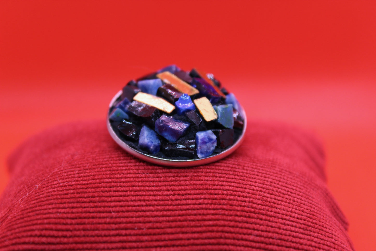 Spilla tonda blu in micromosaico con oro su sfondo rosso