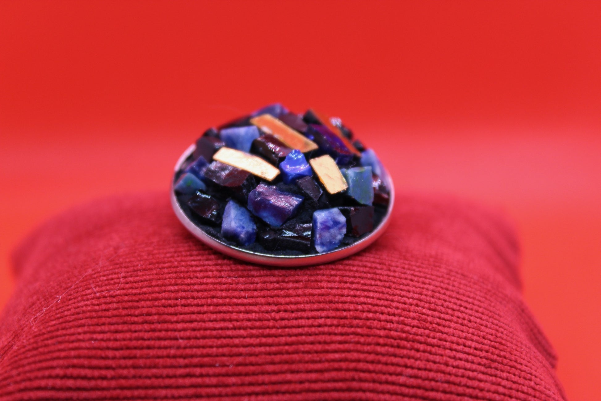 Spilla tonda blu in micromosaico con oro su sfondo rosso